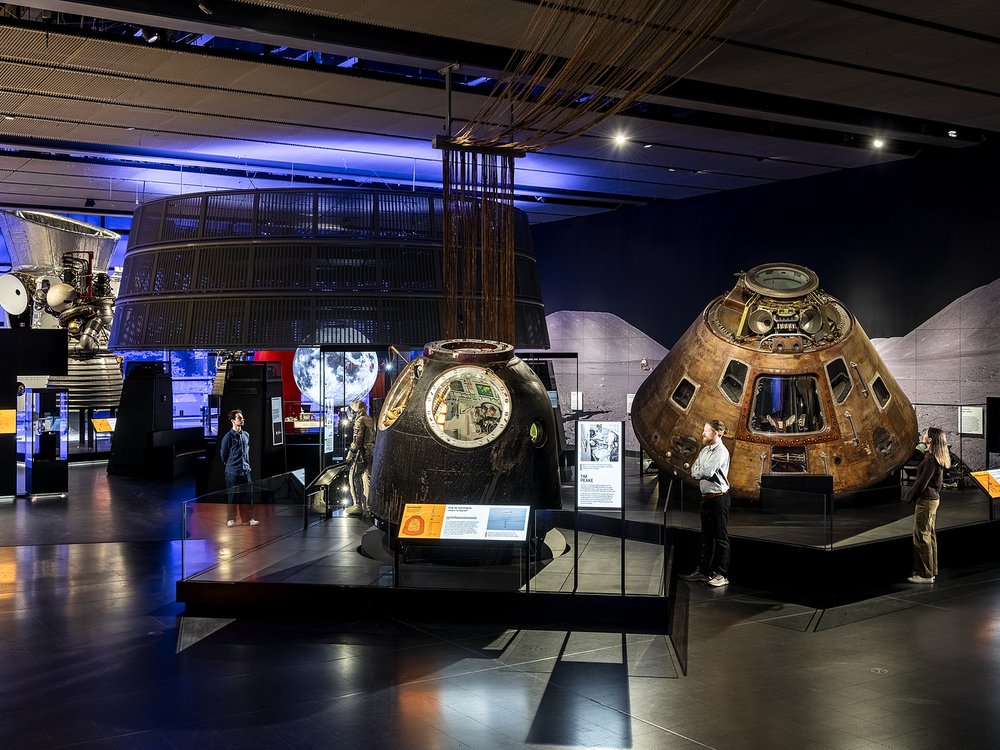 Visitors exploring the Space Gallery at the Science Museum, featuring historic spacecraft and exhibits under dim lighting.