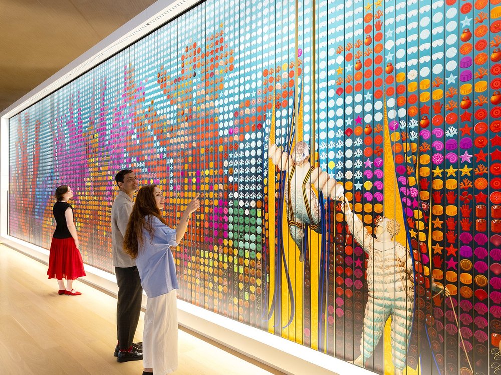 Two visitors looking at a vibrant, colourful large-scale wall installation made of geometric tiles at the Design Museum.