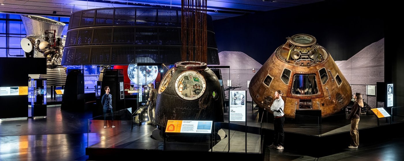 Visitors exploring the Space Gallery at the Science Museum, featuring historic spacecraft and exhibits under dim lighting.