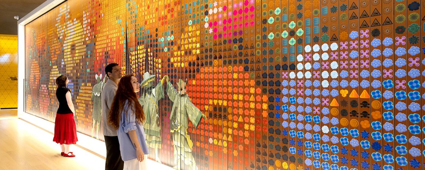 Two visitors looking at a vibrant, colourful large-scale wall installation made of geometric tiles at the Design Museum.