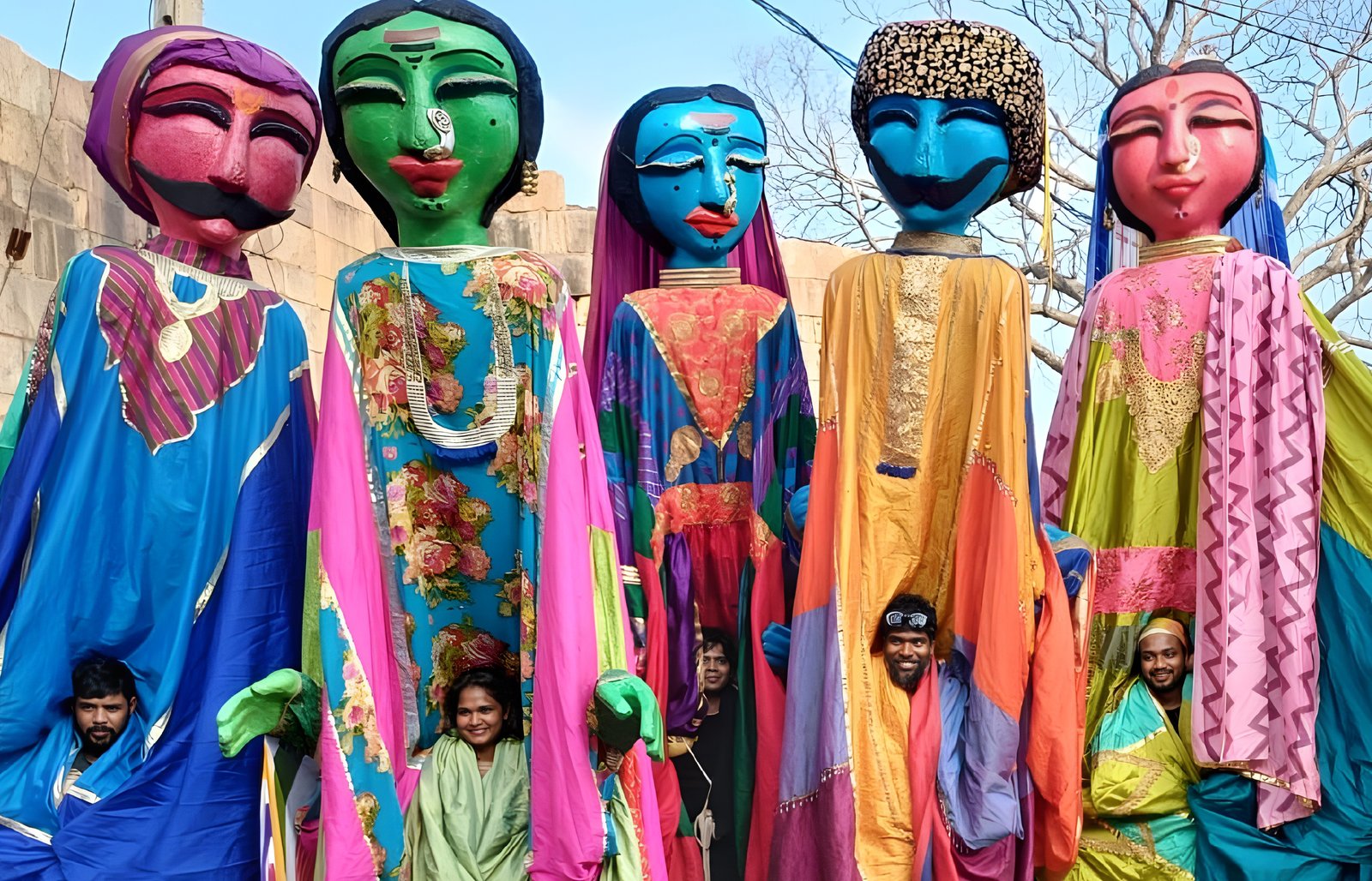 Colourful giant puppets in bright costumes parading outdoors, with performers visible beneath the figures during a cultural festival.